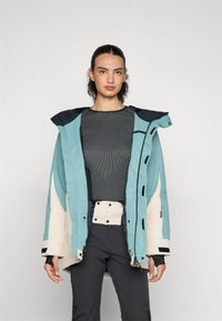 Synthetic blue and cream jacket with a hood, featuring contrast stitching, a zip closure, and adjustable cuffs. Worn over a grey top.