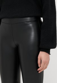Must-have musta faux nahk leggingud on sileda, läikiva viimistlusega ja kõrge vöökohaga. Mudel kannab musta tekstuuriga sviitrit.