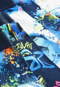 Gros plan d’un tissu avec des motifs abstraits de graffiti en bleu, blanc et noir et des éclaboussures de peinture colorée en orange, jaune et vert.