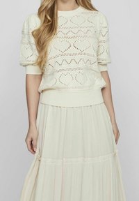 Pletený krémový svetr s motivy srdce a cik-cak, krátkými puff rukávy a žebrovým lemováním. V kombinaci s lehkou, světlou maxi sukni.