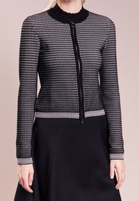 Black and white patterned jacket with a zip closure, ribbed collar, and cuffs. Textured fabric with a fitted silhouette, paired with a black skirt.