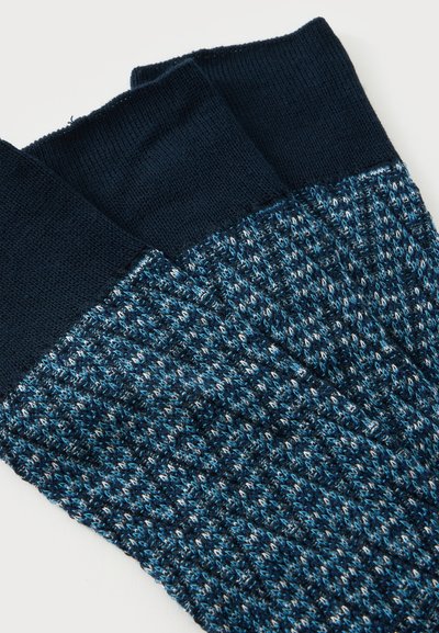 Paire de chaussettes tricotées pliées avec des poignets noirs et un motif moucheté bleu, noir et blanc sur le corps principal.