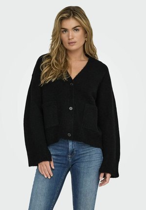 Cardigan nero in maglia con scollo a V, due tasche frontali e chiusura con bottoni. Tessuto testurizzato e maniche ampie. Abbinato a jeans blu.