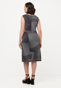 Vestido sin mangas en negro y gris con patrones en forma de olas, cintura ajustada y un dobladillo fluido. Tejido suave con un ligero brillo y cremallera en la espalda.