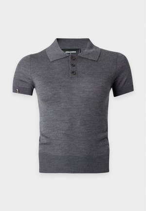 Femme portant un polo gris cintré à manches courtes, une longue jupe marron avec fente devant, une ceinture marron et des sandales noires à talons hauts, debout sur fond blanc.