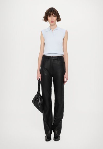 Débardeur sans manches bleu clair avec des boutons, associé à un pantalon large en cuir noir. Le mannequin tient un sac à main noir et porte des chaussures noires.