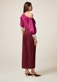 Off-shoulder magenta blouse met ballonmouwen, gecombineerd met hoge burgundy wijde broek en slingbackhakken met luipaardprint.