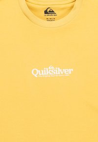 Žlté tričko Quiksilver s bielym logom a textom "Quiksilver The Original Surf Co Since 1969" umiestneným na strede pod výstrihom.