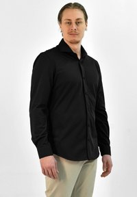 Zwarte lange mouwen shirt van gladde stof, met een knoopsluiting aan de voorkant, kraag en aansluitende manchetten, gecombineerd met lichtgekleurde broeken.