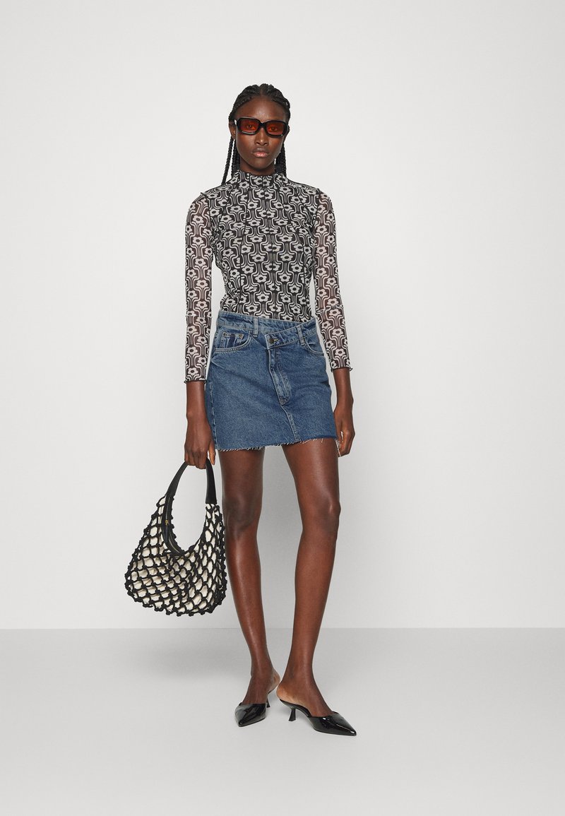 Maglietta a maniche lunghe a fantasia bianco e nero, mini gonna in denim blu, mules a punta nera e borsa a tracolla intrecciata nera.