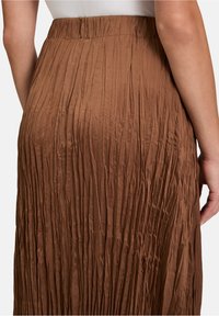 Jupe plissée marron au design fluide, dotée d'une taille haute et d'un tissu texturé, vue de dos. Légère et qui tombe bien.