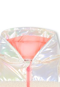 Giacca con cappuccio in tessuto iridescente lucido nella parte superiore, morbido polare crema nella sezione inferiore e interni rosa con una zip a forma di cuore.