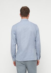 Sininen ja valkoinen ruudullinen pitkähiha paita, jossa on napituskaulus ja hihansuut, valmistettu kevyestä kankaasta. Takakatsauksessa näkyy muotopuoli ja helma.