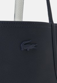 Sac bleu marine texturé au design robuste, avec un logo crocodile noir proéminent et des bords lisses.
