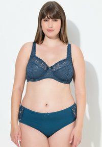 Reggiseno in pizzo blu navy con bordi ondulati e un piccolo fiocco al centro, abbinato a mutandine a vita alta con dettagli in pizzo.