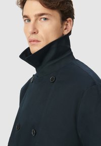 Granatowy dwurzędowy płaszcz z wysokim kołnierzem, z czarnymi guzikami, gładką fakturą i czystymi liniami.