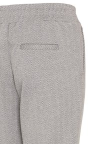 Gros plan d’un pantalon gris à motif chevrons montrant la poche arrière et le détail de la ceinture.