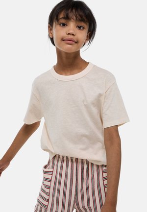 T-shirt en coton beige clair avec un col rond et des manches courtes, associé à un pantalon beige rayé avec des détails rouges et verts.