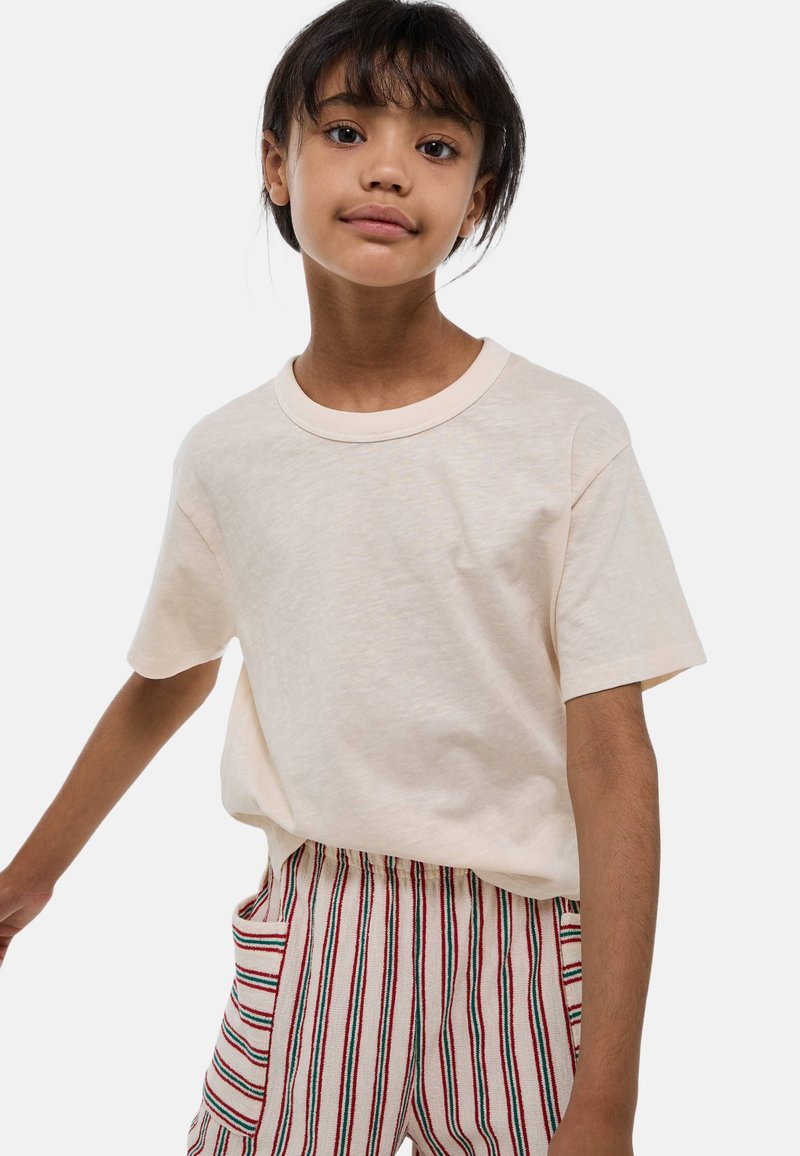 T-shirt en coton beige clair avec un col rond et des manches courtes, associé à un pantalon beige rayé avec des détails rouges et verts.