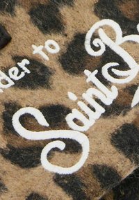 Il tessuto a fantasia leopardata presenta macchie marroni e nere; il testo ricamato in bianco recita "Saint". L'attenzione è rivolta ai dettagli della texture e del pattern.
