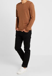 Chemise longue manches en brown en tricot texturé, associée à un jean noir et des baskets blanches. La chemise a un col rond.