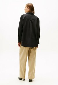 Zwarte langermige shirt met een eenvoudige kraag en knoopmanchetten, gecombineerd met beige wijde broek. Glad stof, minimalistisch ontwerp.