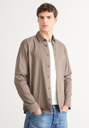 Brown-striped button-up shirt in lightweight fabric, featuring a collar, long sleeves, and black buttons, paired with a plain white t-shirt.