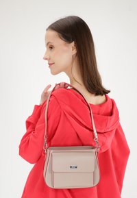 Beige håndtaske med kontrasterende rød syning, rektangulær form, glat syntetisk materiale og en kort skulderrem.