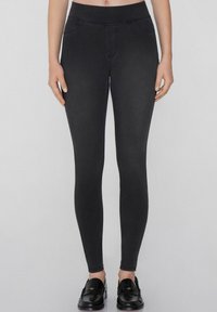 Jeggings negros con una cinturilla alta, que presentan una textura suave, bolsillos falsos y una silueta ajustada. Combinados con mocasines negros.