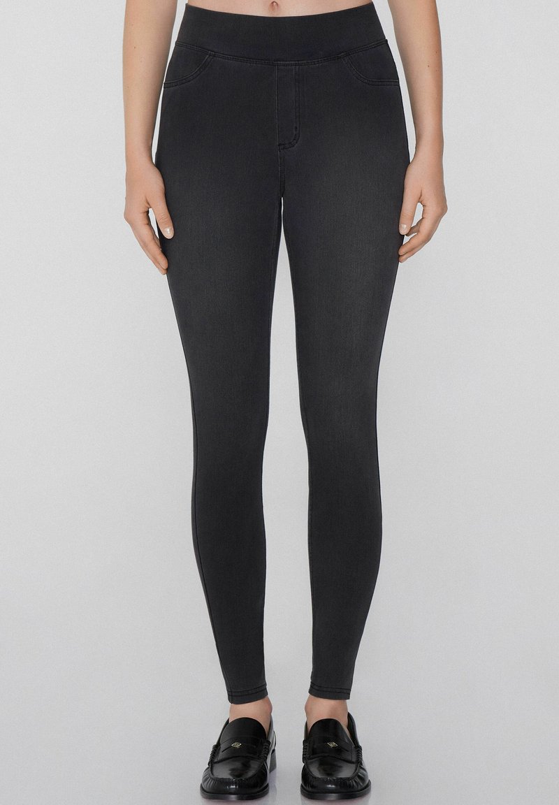 Jeggings negros con una cinturilla alta, que presentan una textura suave, bolsillos falsos y una silueta ajustada. Combinados con mocasines negros.