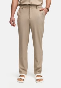 Beige, geribde broek met een rechte pasvorm, voorzien van een riemlus met knoopsluiting en zijzakken, gecombineerd met witte sandalen.