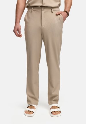 Beige, ribbed trousers with a straight leg fit, featuring a belt loop with a button closure and side pockets, paired with white sandals.