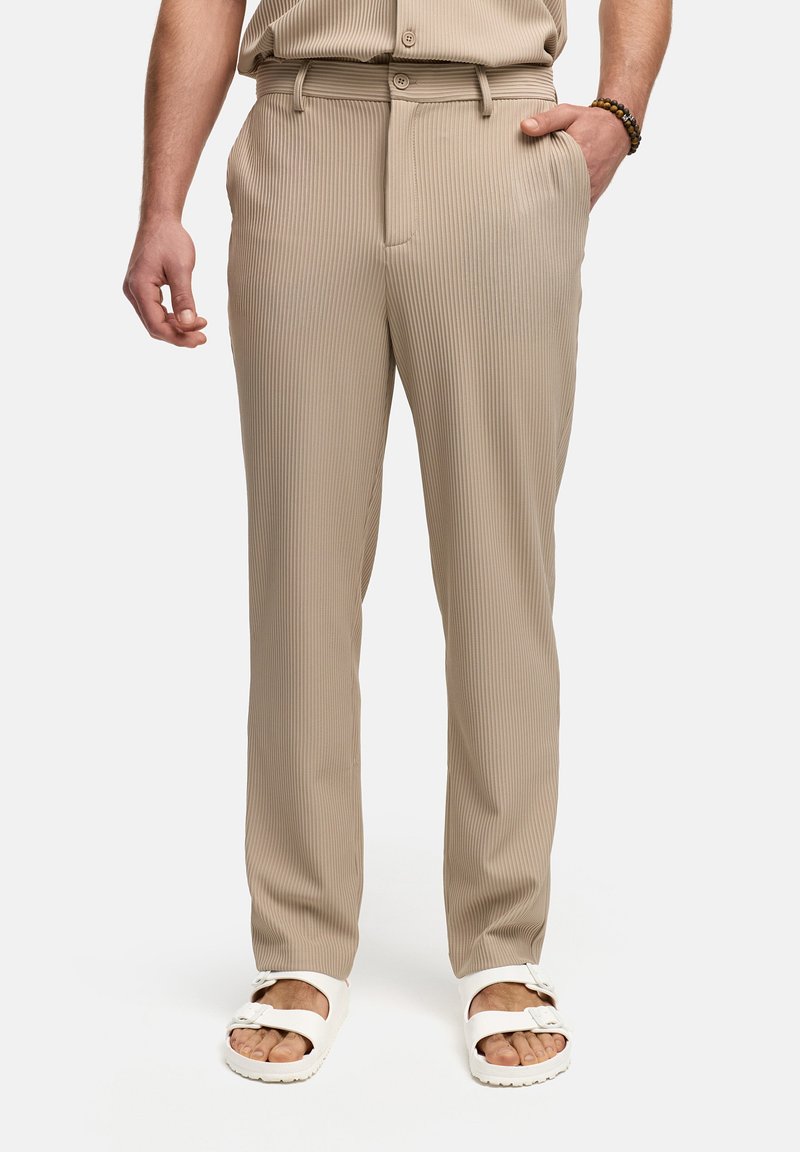 Beige, geribde broek met een rechte pasvorm, voorzien van een riemlus met knoopsluiting en zijzakken, gecombineerd met witte sandalen.