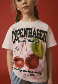 Hvid bomulds T-shirt med grafisk print af kirsebær på en lyserød ternet baggrund. Teksten inkluderer "COPENHAGEN Fruit Market."