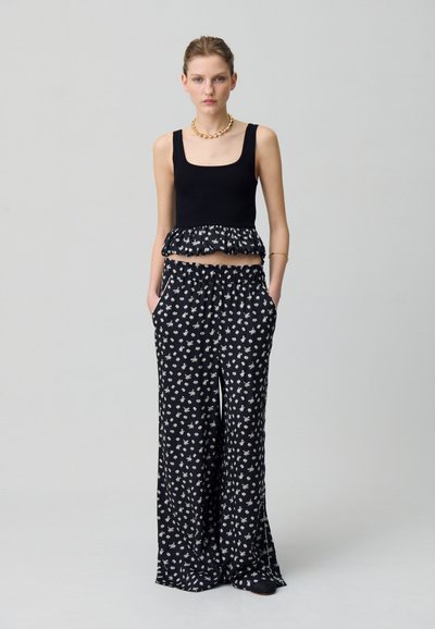Top crop nero con orlo volant, abbinato a pantaloni neri larghi con piccoli motivi floreali bianchi e tasche laterali.