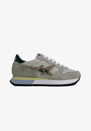 Scarpa sportiva beige realizzata in suede e rete, con un logo dorato glitterato, lacci bianchi e un tallone nero su una suola a contrasto.