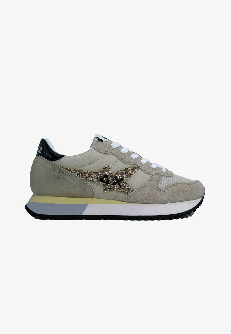 Scarpa sportiva beige realizzata in suede e rete, con un logo dorato glitterato, lacci bianchi e un tallone nero su una suola a contrasto.