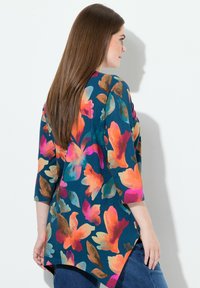 Tunic floreale multicolore con maniche a tre quarti, caratterizzata da colori vivaci come arancione, rosa e verde acqua su uno sfondo scuro.