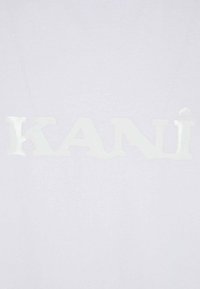 White T-shirt featuring a large, glossy, white graphic that spells "KANÍ" in a bold, stylized font without any additional patterns or textures.