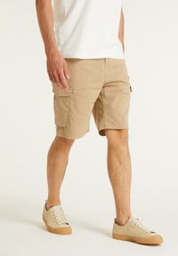 Shorts cargo kaki avec plusieurs poches, une coupe ample et un tissu en coton lisse. Associés à des baskets beiges avec des semelles texturées.