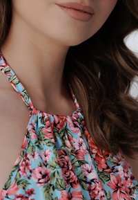 Kvetinový halter top s modrou látkou a ružovými a červenými kvetmi, zhromaždený výstrih a tenké ramienka. Hladká textura a živé farby.