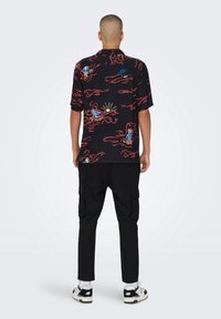 Korte mouwen zwarte shirt met kleurrijke golf- en zonpatronen, met een relaxte pasvorm en een detail van een achterzak. Gecombineerd met zwarte cargobroek.