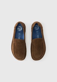 Καφέ παπούτσια τύπου slip-on από σουέντ με ομαλή υφή, στρογγυλερή μύτη και μπλε εσωτερική σόλα με λογότυπο. Απλός σχεδιασμός, χωρίς ορατά μεταλλικά στοιχεία.