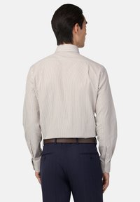 Camisa de vestir a rayas en crema y marrón con mangas largas, cuello clásico y puños con botones, combinada con pantalones azul marino y un cinturón marrón.