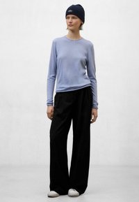 Top de manga larga azul claro, pantalones de pierna ancha negros y zapatillas blancas. La modelo lleva un gorro azul oscuro. Textura suave, corte relajado.