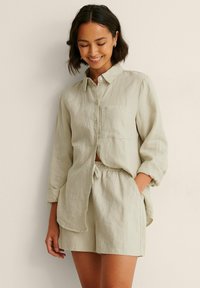 Light green linen shirt with a button-down design, long sleeves, and single chest pocket paired with matching drawstring shorts.