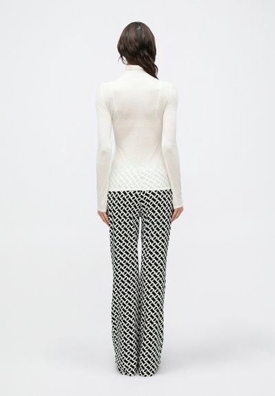Λευκό τοπ με μακριά μανίκια σε συνδυασμό με ασπρόμαυρο παντελόνι καμπάνα με γεωμετρικά σχήματα και απαλό, ελαφρύ ύφασμα.