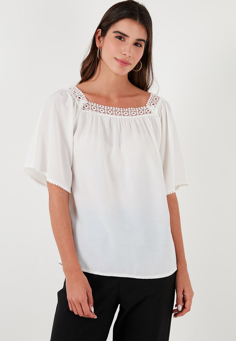 White blouse featuring short flutter sleeves, a square neckline adorned with crochet detailing, and lightweight, textured fabric.