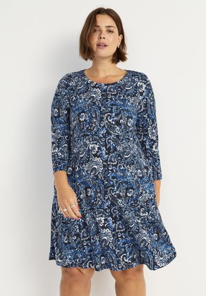 Sininen paisley-kuosiset mekko, jossa on pyöreä pääntie ja kolmannesosa hihat. Pehmeää kangasta ja virtaava siluetti.