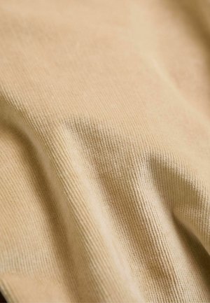 Beiger Stoff mit einer gerippten Textur, der weiche, leicht glänzende Fasern zeigt. Das Layout ist drapiert und betont den Fluss und die Konturen des Materials.